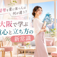 大阪城と通天閣を望む明るい部屋で、ノートを持つ上品な女性が自然体で立ち、大阪で姿勢を楽に保つための重心と立ち方の大切さを示している。